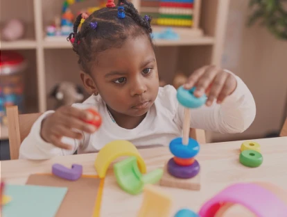 A young girl stacking colorful rings on a peg in a classroom.